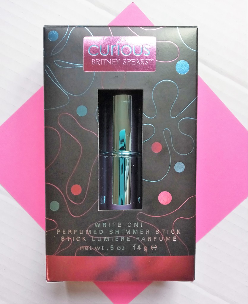 The Curious solid perfume stick in its box, against a pink and white background