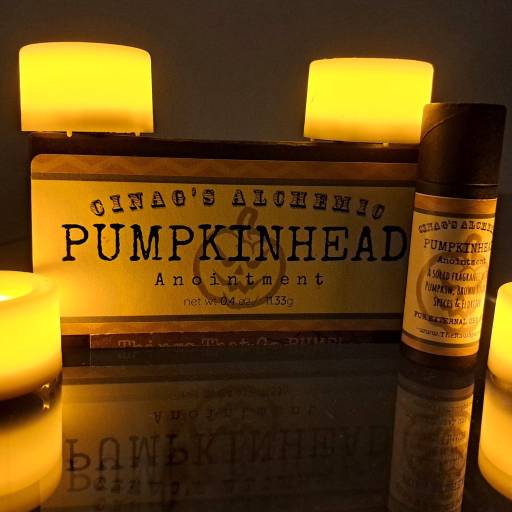 The Pumpkinhead box and perfume stick, in a dimly-let environment, next to burning candles, with the label reflected in the glass of the table